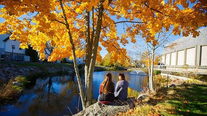 Two students sitting outside on campus in the fall. 